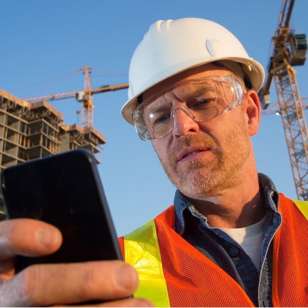 Bauarbeiter schaut aufs Handy